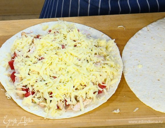 На тортилью выложить куриную начинку, посыпать натертым сыром и накрыть сверху второй лепешкой.