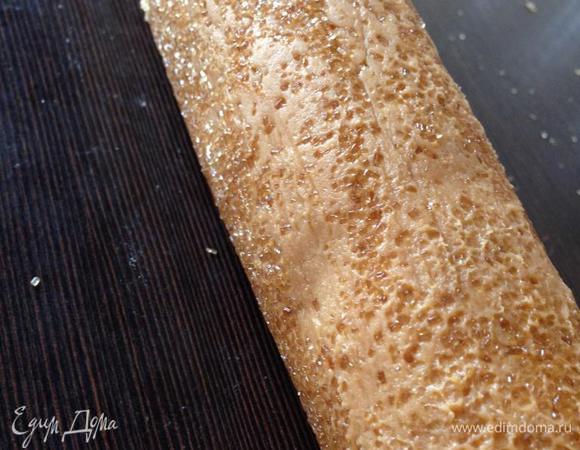 По истечении времени разогреваем духовку до 180 градусов. Достаем схватившееся тесто, убираем пленку и обваливаем колбаску в сахаре, равномерно рассыпанном на рабочей поверхности. Просто катаем тесто по столу как скалку...