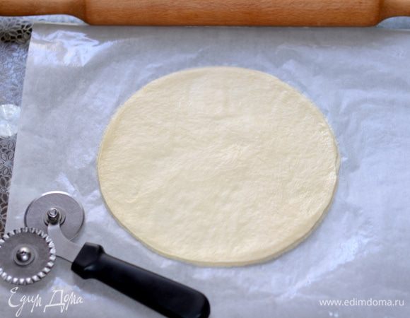 Тесто выложить на рабочую поверхность, обмять руками. Разделить на 2 части, накрыть салфеткой. Одну часть теста раскатать в круг толщиной примерно 1,5 см.