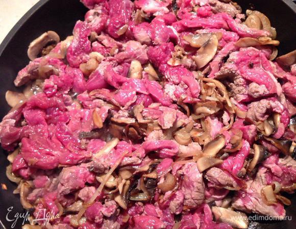 Лук и грибы тушим на разогретом масле до золотистого цвета, затем добавляем мясо. Перемешиваем и продолжаем обжаривать на среднем огне.