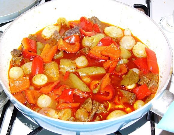 Когда мясо по мягкости приближается к готовому, добавляем в сотейник ощищенный лук-шалот, нарезанный перец, очиценные зубчики чеснока, 1 нарезанный помидор. Если есть томаты в собственном соку, добавляем вместо свежего помидора их. Хорошо приправить блюдо специями для мяса и тушения. Посолить. 