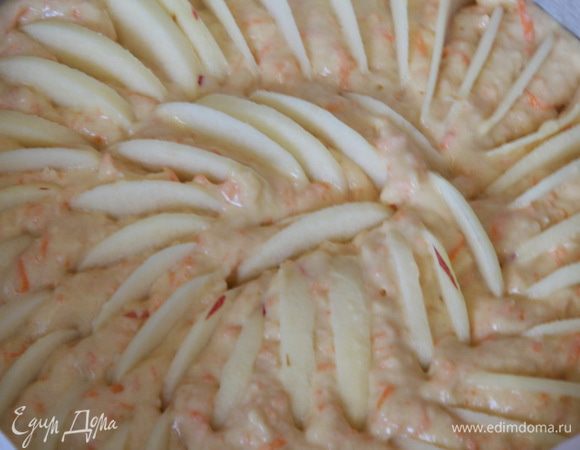 Форму диаметром 22 см выстилаем бумагой для выпечки и перекладываем в форму тесто. Оставшиеся два яблока чистим и нарезаем тонкими пластинами. Яблочные пластины вдавливаем в тесто.