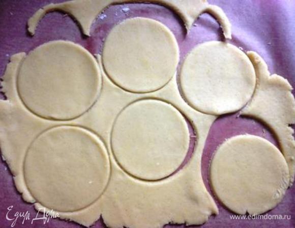 Тесто разделить на 2 части и 1 из них раскатать на пергаменте, круглой выемкой вырезать заготовки.