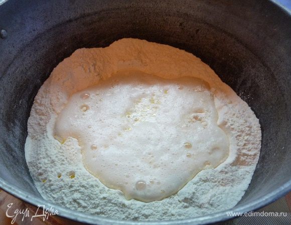 В глубокую кастрюлю просеиваем муку, выливаем подошедшие дрожжи, растопленное сливочное масло и добавляем подсолнечное масло.