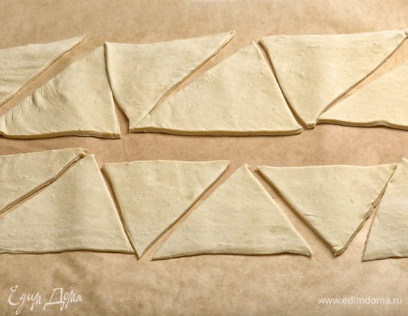 Тесто достать из холодильника и раскатать в прямоугольник, накрыть полотенцем, оставить на 10 минут. Затем тесто разрезать вдоль пополам.  Каждую из получившихся частей нарезать на равные треугольники.

