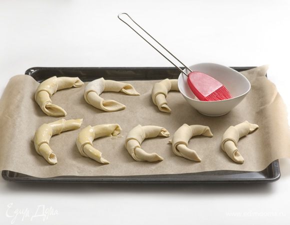 Из получившихся треугольников свернуть круассаны, придать им форму полумесяца и выложить на противень, предварительно застеленный бумагой для запекания, захлестами вниз. Расстояние между круассанами оставить минимум 5 см. Смазать круассаны взбитым яйцом и оставить на 40 минут для поднятия. Выпекать круассаны около 20 минут при температуре 180-200°C.
