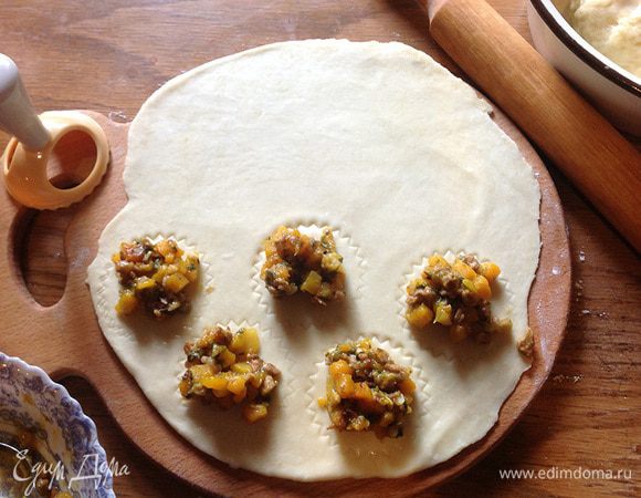 На слегка присыпанной мукой поверхности раскатать часть теста, не слишком тонко, 4-5 миллиметра толщиной. На одной половине наметить формочкой для равиоли или просто узким бокалом кружки. В эти кружки выкладывать начинку по чайной ложке.