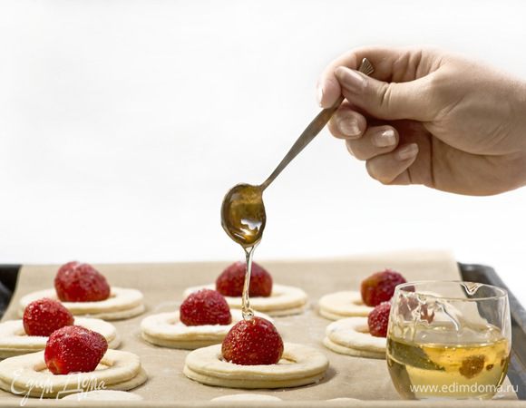 Противень выстелить бумагой для выпечки, выложить большие кружки теста, сверху каждого кружка уложить колечки из теста. В середину каждого кружка поместить ягоду клубники, посыпать ее щепоткой сахара и полить небольшим количеством меда.
