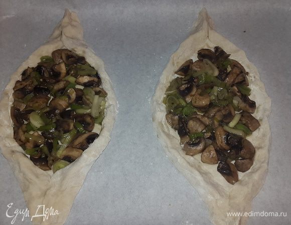 Размороженное тесто присыпаем мукой, слегка раскатываем или формируем пальцами форму овала.  Выкладываем в центр начинку, формируем лодочки с бортиками. Выкладываем на застеленные пекарской бумагой противни.