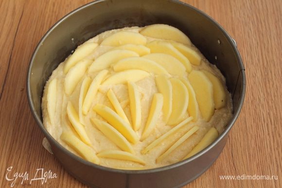 Тесто выложите в форму. Яблоки очистите, нарежьте тонкими дольками. Вдавите дольки в тесто.