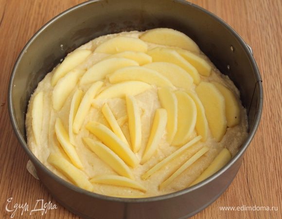 Тесто выложите в форму. Яблоки очистите, нарежьте тонкими дольками. Вдавите дольки в тесто.