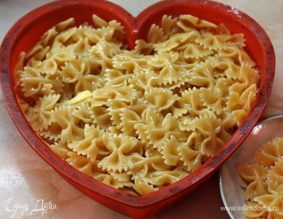Макароны отварить до готовности, слить воду (я отложила небольшое количество бантиков для украшения, но это не обязательно). Выложить макароны в форму для запекания(ку меня силиконовая), добавить сливочное масло и перемешать. Дать им немного остыть. Включить духовку на разогрев до 180 градусов.