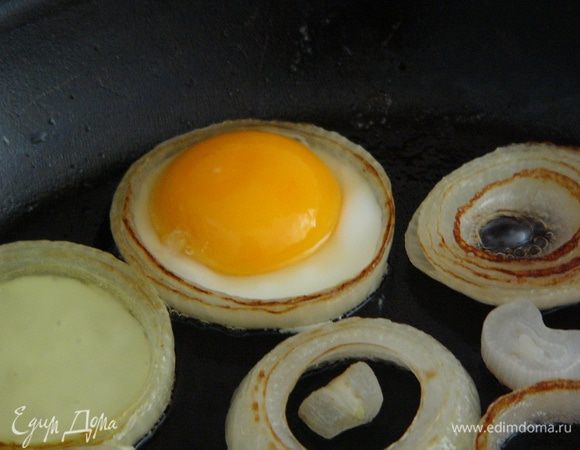 Внутрь крупных колец лука разбиваем яйцо (для удобства можно сначала разбить яйцо в чашку, убедившись, что желток не поврежден, и переложить его на сковороду ложкой). Жарить под крышкой еще пару минут, пока желток не схватится.