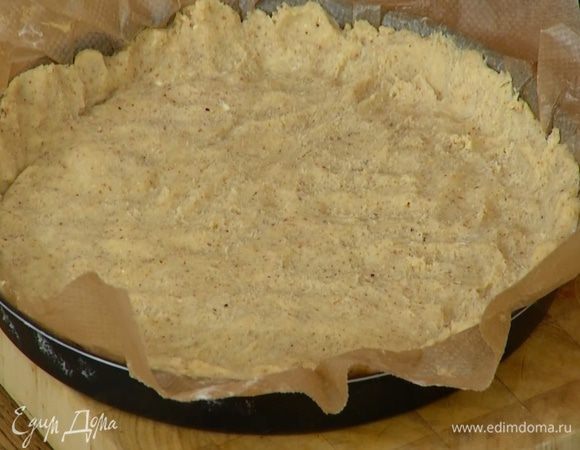 Бумагу для выпечки смазать половиной сливочного масла и распределить на ней большую часть охлажденного теста слоем примерно в сантиметр толщиной, затем уложить бумагу с тестом в форму и сформировать из теста бортики.