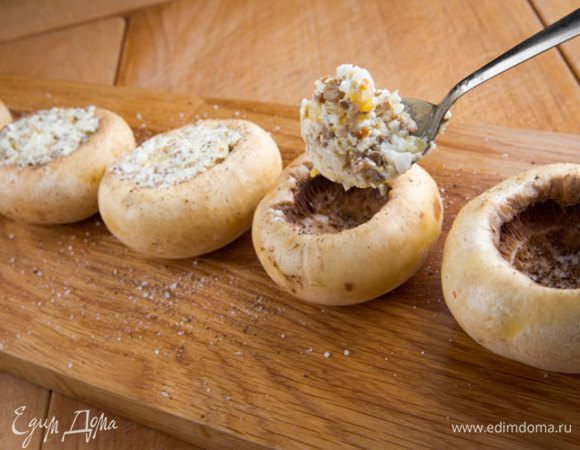 Шляпки грибов посолить и поперчить по вкусу, смазать оливковым маслом и наполнить приготовленной начинкой. Форму для запекания смазать маслом, выложить грибы, положить в каждую шляпку кусочек сливочного масла.