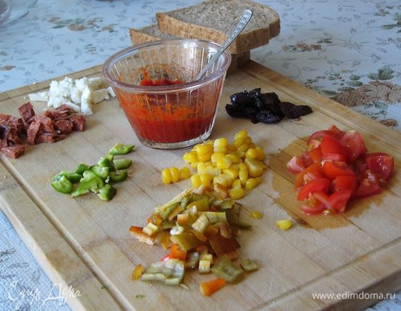 Подготовим необходимые продукты для пиццы: сыр, помидоры, перец, маслины или какие любите вы. Если хотите, подготовьте сосиски, ветчину или колбаски. Все мелко нарежем. У меня еще нашлась кукуруза. 
Перцовую пасту (можно заменить томатной) смешаем с оливковым маслом. 
Подготовим 3 кусочка черствого хлеба. Подойдет любой, какой у вас есть. 
Духовку включаем разогреваться до 180°С. 