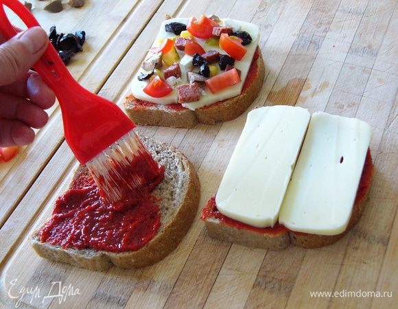 С помощью кисточки намажем хлеб перцовой пастой. Сверху положим пластины сыра. На сыр разложим начинку. Положим сверху несколько кусочков моцареллы или брынзы. 