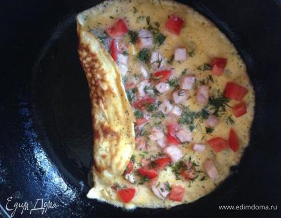 Как только омлет немного схватится, начинаем его сворачивать в рулетик.