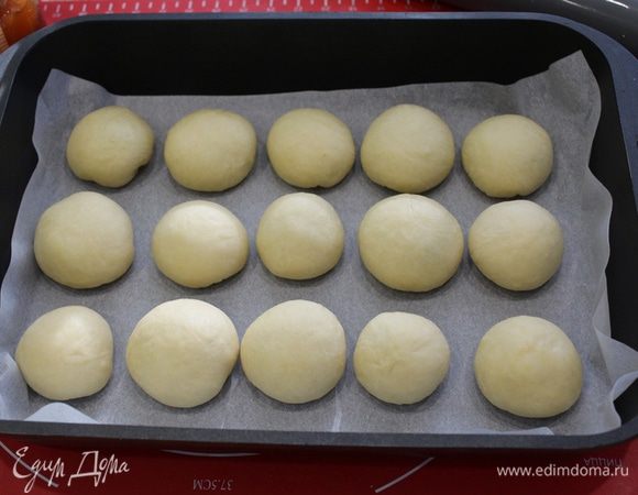 Форму для выпечки выложить пекарской бумагой, расположить булочки, оставляя расстояние между ними.