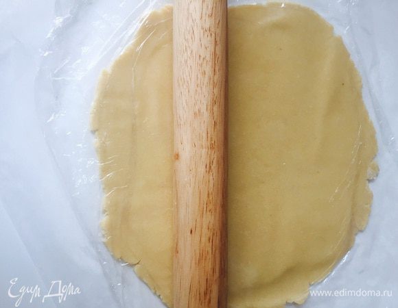 Достаем песочное тесто. Выкладываем его на бумагу для выпечки, опять накрываем пленкой и раскатываем в тонкий пласт 4-5 мм. Потом переносим тесто прям на бумаге на противень, ставим на него нашу форму для торта (в идеале квадратная 18/18, у меня круглая д 22), хорошенько надавив, и прям так отправляем в духовку на 10 минут.