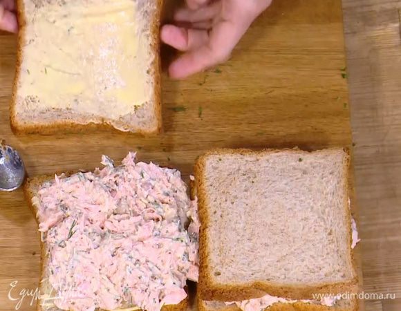 Куски хлеба смазать половиной сливочного масла, на два из них выложить рыбную начинку, равномерно распределить и накрыть оставшимся хлебом маслом вниз.