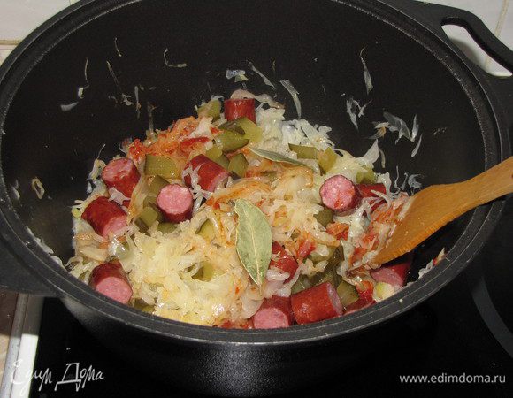 За 15-20 минут до готовности капусты, добавить томатную пасту, нарезанный соленый огурец и охотничьи колбаски. Перемешать.