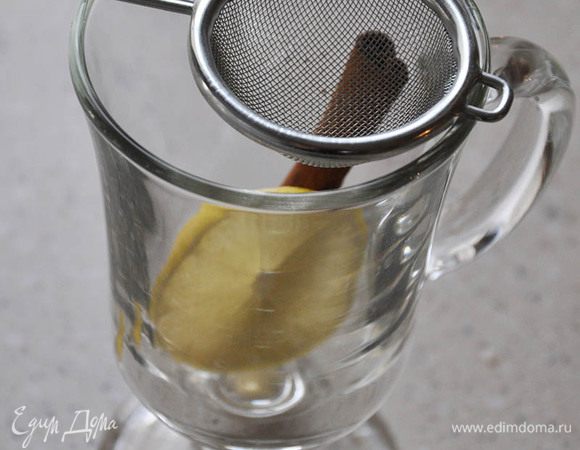 В бокал добавить большую дольку лимона и сахар. Через ситечко процедить глинтвейн. Размешать. Положить палочку корицы из кастрюльки.