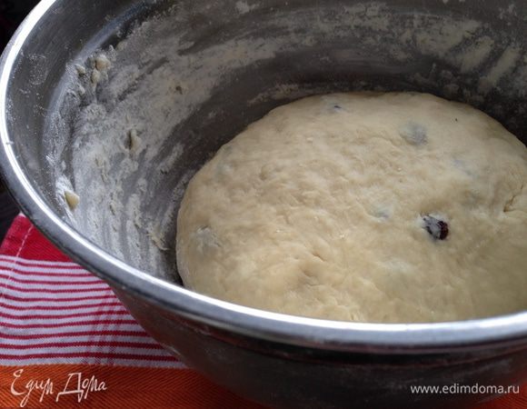 Постепенно добавить просеянную муку и изюм. Тесто вымешать в течении 10 минут. Оно должно получится гладким, но слегка липнущим. Положить тесто в миску, накрыть пищевой плёнкой и убрать в тёплое место на 1,5-2 часа для подъёма.