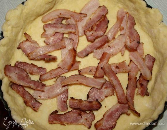 Большую часть теста раскатываем и укладываем в форму 20 см. Ломтики бекона рвем на кусочки и укладываем на тесто.