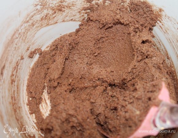 В масляную смесь частями всыпать сухие ингредиенты и смешать лопаткой. Добавить шоколад. и перемешать. Форму 20 см смазать маслом, выложить тесто.