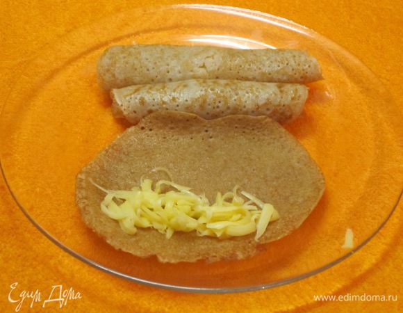 Выложить тертый сыр на каждый блинчик. Можно добавить мелко нарезанную ветчину. Свернуть в рулетики.