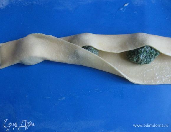 Промежутки между ними смазать кисточкой взболтанным белком, так же поступить с одной длинной (ближней к вам) стороной, которая будет последней при заворачивании начинки. Другую длинную сторону смазывать белком не надо.
Заверните дальнюю от вас длинную сторону на начинку, она прикроет ее примерно наполовину, теперь ближней длинной стороной теста накройте начинку и частично тесто.


