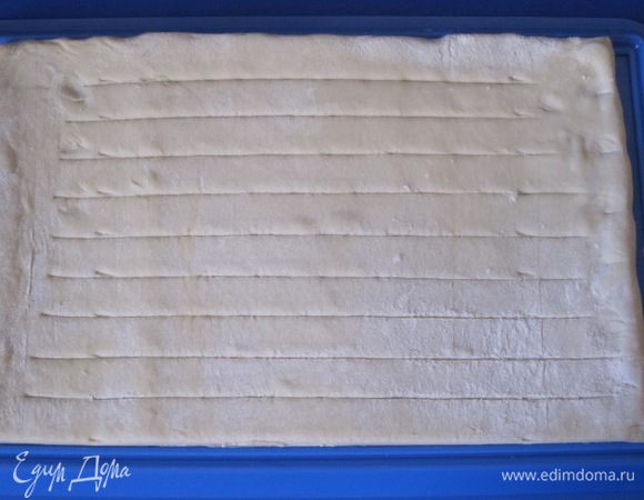 Тесто разморозить, раскатать. Сделать надрезы на расстоянии 1,5 см друг от друга, не дорезая до края.