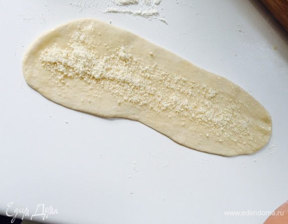 Раскатываем в тонкий узкий пласт толщиной 3-4 мм. Смазываем растопленным сливочным маслом, посыпаем пармезаном.