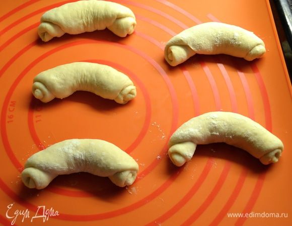 Из остальных кусочков теста (вторая половина) можно сформировать рогалики. Для этого шарик-заготовку поверните швом вверх. Раскатайте в продолговатую лепешку. Слегка растягивая край скрутите в рогалик. Прокатайте... Готовый рогалик слегка припылите мукой. И придайте форму подковы. Рогалики тоже выложите на противень, застеленный пекарской бумагой для расстойки на 50 мин. швом вниз. Прикройте...