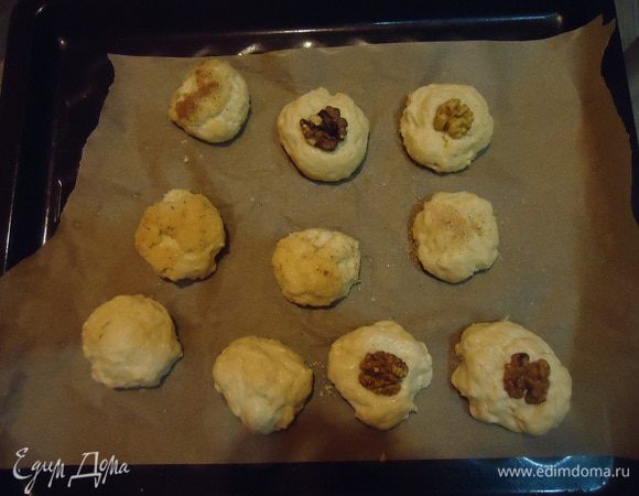 Ставим греться духовку на 220°С. 
Столовой ложкой берём кусочек теста и катаем шарик смоченными водой или подпылёнными мукой руками. Выкладываем на пергамент. Я часть обмакнула в корицу с сахаром, часть — украсила орешками.