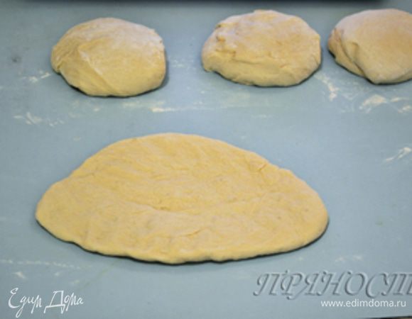 Затем берем первый шар, припыляем рабочую поверхность мукой,  переворачиваем гладкой стороной вниз и ладонями придаем тесту форму неправильного овала.