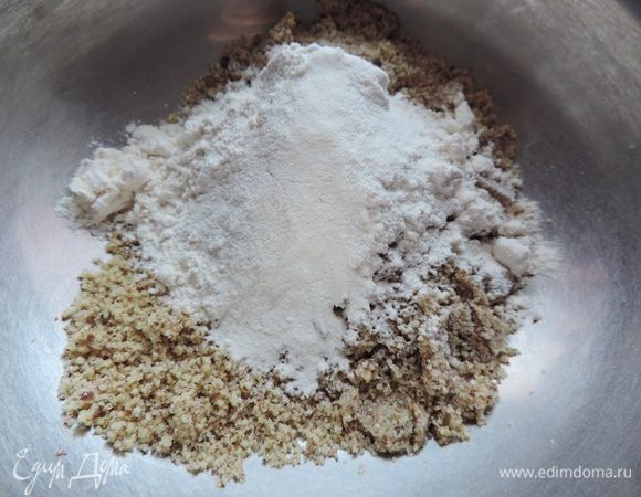 Первым делом подготовим грецкие орехи. Их нужно измельчить максимально мелко. Чтобы во время измельчения орехи не превратились в маслянистую кашицу, добавьте к ним пару чайных ложек сахара из общего количества.
В емкость с измельченными орехами добавляем муку и разрыхлитель.