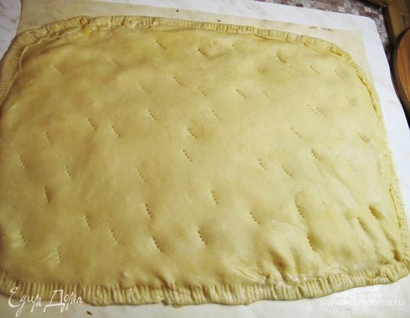 По своей структуре оно близко к вытяжному тесту. И так же хорошо раскатывается. Хорошо посыпаем доску для раскатки мукой. Толщина листа около 3-4 мм. Я обычно раскатываю его на обычной доске, подпыленной мукой, затем переношу на скалке на противень. Можно раскатывать и на бумаге для выпечки и переносить вместе с ней. Кому как удобно. Можно выпекать и без бумаги для выпечки, ничем не смазывая противень.
Нижний лист должен быть чуть больше верхнего. Намазываем начинку, закрываем верхним листом и хорошо защипываем края. Я обычно загибаю нижний лист по краю наверх и прохожу сверху вилкой для лучшего соединения.