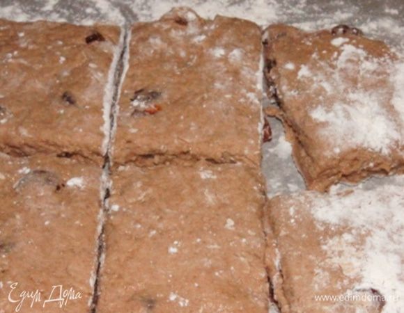 Распределить тесто руками на столе присыпанном мукой. Разрезать поперек на 2 части, а потом на квадраты.