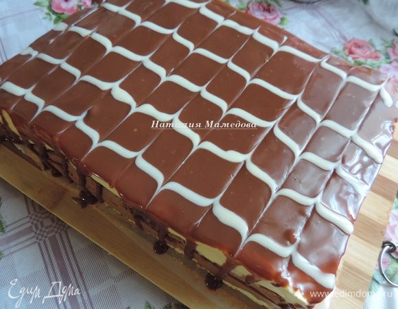 Пока глазурь не застыла, можно сделать узор из растопленного белого шоколада. Нанесите полоски белой глазури вдоль большей стороны прямоугольника, а затем зубочисткой проведите линии, параллельные меньшей стороне торта, на одинаковом расстоянии. Один раз зубочистку ведем от нижнего края торта к верхнему, следующую линию наоборот — от верха торта к низу. Таким образом мы получим красивый узор. 