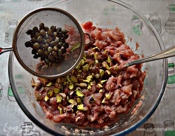 Добавьте к фаршу фисташки и каперсы, жидкость от которых нужно предварительно слить. У меня каперсы были в соли, поэтому я предварительно хорошо промыла их в тёплой кипячёной воде. В принципе, если у вас нет каперсов, то их можно заменить на порезанные на кусочки оливки. 
Фарш хорошо перемешайте.