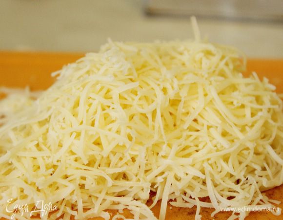 Сыр натереть на мелкой терке. Половину сыра добавить в горячий соус и хорошенько перемешать.