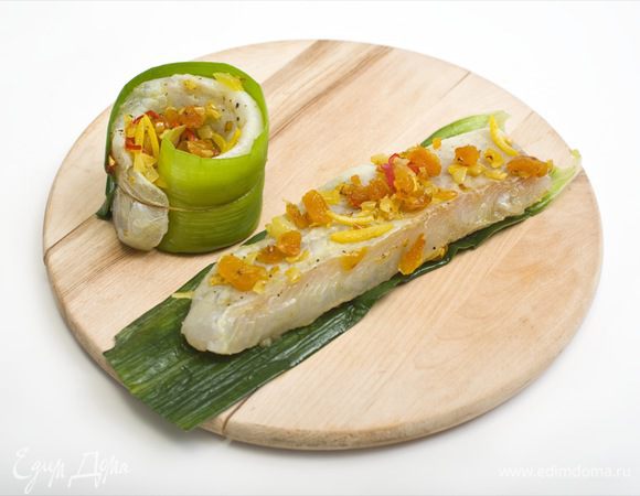 Листья лука порея выложить на разделочную доску, сверху на каждый лист поместить рыбное филе и аккуратно свернуть рулетики.
