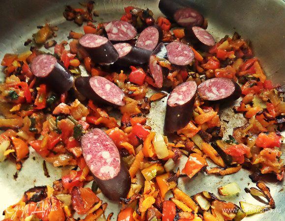 Нарезать наискосок в сковороду колбаски. Помешать на огне.