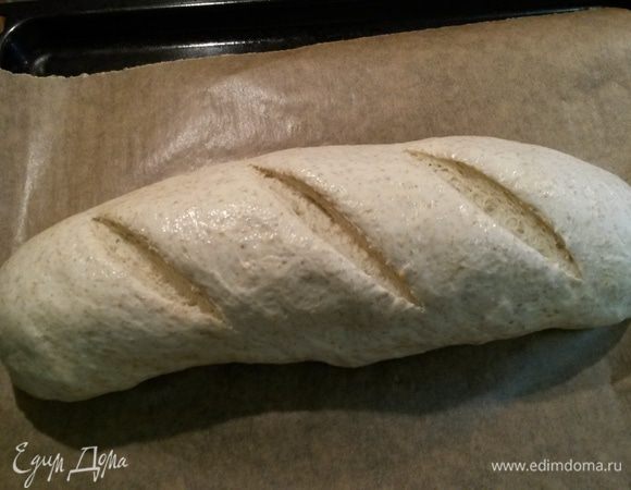 Духовку разогреваем до 240°C. Батон смачиваем водой (кистью или мокрой ладонью). Делаем на батоне надрезы хлебным ножом или лезвием (3 или 5 полос). Убираем хлеб в духовку на 30 минут. Температуру духовки уменьшаем до 200°C. Первые 10 минут печем с паром.
Что значит печь с паром? На дно духовки ставим металлическую миску или чугунную сковороду (у меня сковорода). Она разогревается вместе с духовкой. Заранее кипятим чайник. Отправляем хлеб в духовку. Сразу же выливаем в миску (сковородку) примерно стакан кипятка и быстро закрываем духовку. Через 10 минут миску с остатками воды убираем из духовки. 
Будьте аккуратны, берегите руки, не обожгитесь паром!