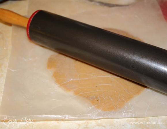 Включить духовку на 175°C.
Остывшее тесто раскатать скалкой. Толщина — на ваш вкус. Если хрустящего и сухого охота, то 2-3 мм, а если пушистого и мягкого, то 8-10 мм будет достаточно. Раскатывать действительно удобно между двумя слоями пергамента — тесто не прилипает к скалке и столу.