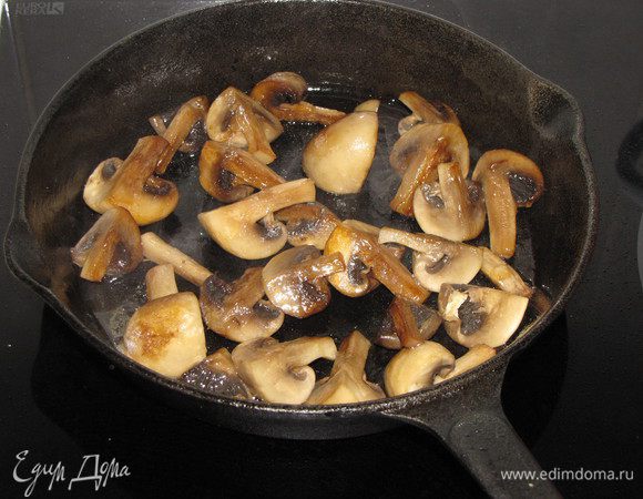 Пока мясо запекается, приготовим грибы. Разрезать крупные шампиньоны на 4 части, мелкие пополам или оставить целиком. Разогреть в сковороде растительное масло и обжарить шампиньоны до готовности, постоянно помешивая, чтобы получить золотистый цвет.