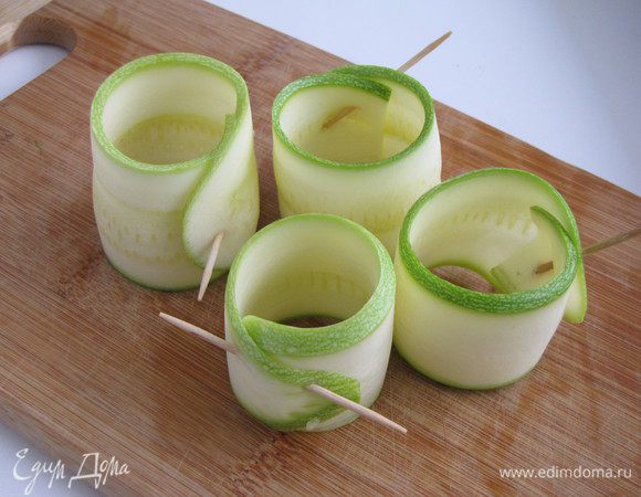 Полоски цукини скрутить в полые рулетики и сколоть шпажкой.