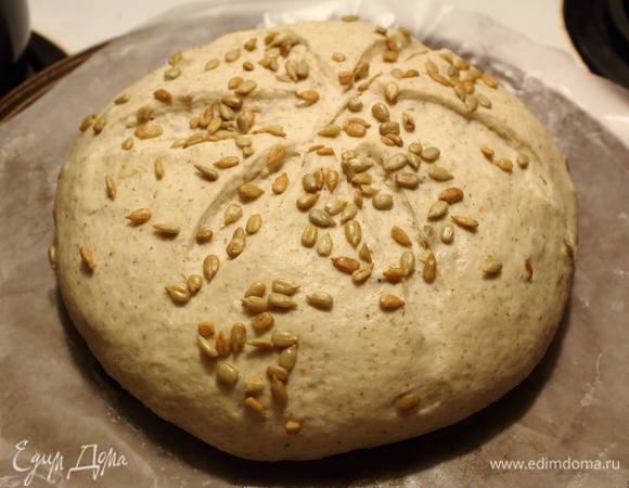 Поднявшееся тесто обмять, уложить на противне на пергамент, смазанный маслом, разрезать сверху будущий хлебушек и обсыпать оставшимися семечками. Снова укрыть хлебушек и поставить его подходить еще на полчаса в теплое место.
